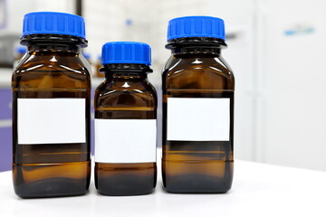 Selective focus of three dark glass reagent bottle with unknown clear liquid chemical inside and blank label in a chemistry laboratory.