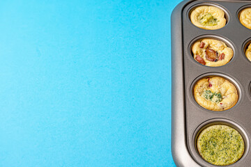 Egg bites with bacon and broccoli in a metal form on a blue background with space for the text on the left