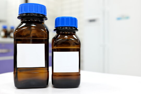 Selective focus of two dark glass reagent bottle with unknown clear liquid chemical inside and blank label in a chemistry laboratory