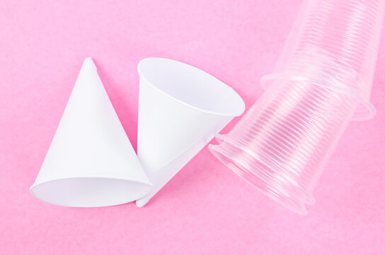 Disposable paper cone water cups and plastic water cups on pink background.