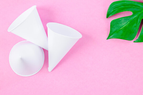 Disposable paper cone water cups with green leaf on pink background.