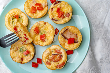 Egg cupcakes for breakfast with bacon and red pepper on a blue round plate with a white tablecloth and chrome fork