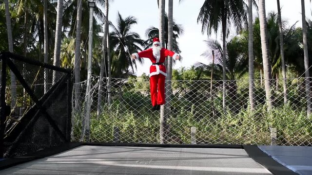 Santa is jumping on a trampoline. Boy in Santa Clause suit makes blanche jump. New Year and Christmas content.  A young man does flip and Santa's beard flies off. Slow motion