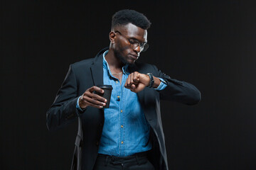 Portrait of american african businessman holding a coffee cup and looking at his watch isolated on black background