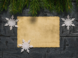 A sheet of antique paper with paper snowflakes and fir branches on a wooden background.