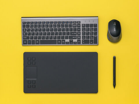 Graphic tablet, wireless keyboard and mouse on a yellow background.
