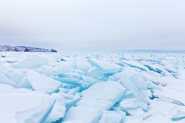 Frosen Lake Baikal on a cold February day. Boundless ice fields of snow-covered hummocks of pieses of blue ice near the snowy Olkhon Island. Winter travel. Natural background