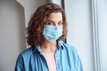 Close-up portrait of young woman in protective mask looking at camera indoors.