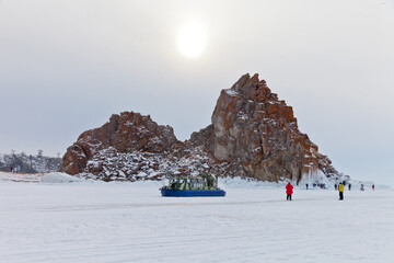 Frozen Baikal Lake on a snowy winter day. A group of tourists arrived in Hivus to the famous Shamanka Rock on Olkhon Island to take pictures of the natural landmark. Ice travel, winter holidays