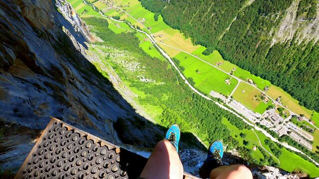A man sits on a platform for base jumpers and people with wing suits. He is looking around.  Underneath is the valley of lauterbrunnen in Switzerland. Its at an altitude of around 800m.