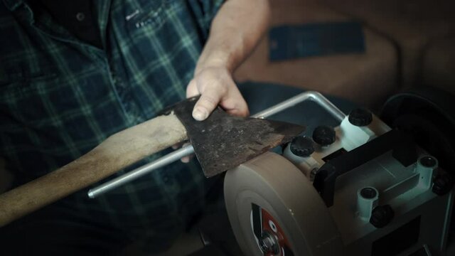 Man sharpening axe on a grinder. Hand close up
