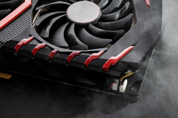 close up broken graphics card with smoke on foreground and dark background. overheating gpu hardware after overclocking. graphic card service concept
