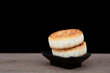 Two Mid-Autumn Festival moon cakes on a small plate in front of a black background