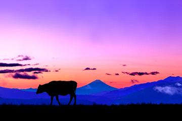 朝焼けの空に富士山のシルエットを背景に、高原の牧場を歩く牛のシルエット