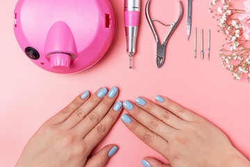 Female hands with blue manicure and manicure tools on pink background top view.