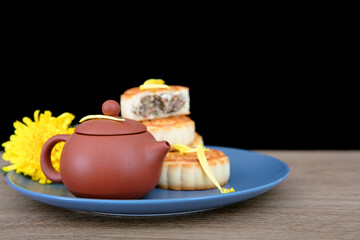 Plate full of moon cakes and a pot of tea and autumn chrysanthemums on the table in front of black background