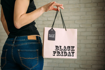Cropped view sexy woman in denim holding paper bag with tag in her hand against a white brick wall...