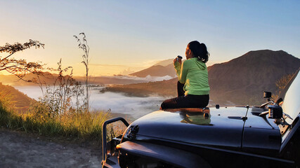 Woman sit on car hood while enjoy mount batur view