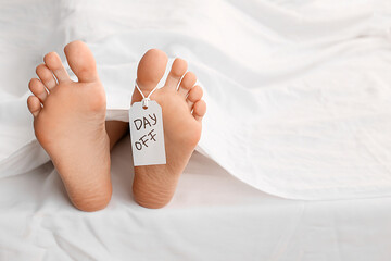 Tag with text DAY OFF on female barefoot legs lying in bed