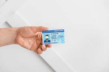 Male hand with driving license on light background