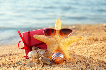 Starfish, sunglasses, decor and gift on beach sand. Christmas vacation concept