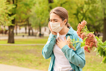 Young woman in medical mask suffering from pollen allergy outdoors