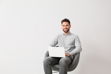 Male psychologist with laptop sitting in armchair on light background