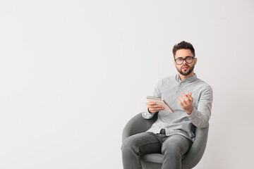 Male psychologist sitting in armchair on light background