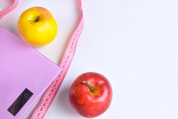 Two apples lie near the electronic scale, and around them lies a measurement for measuring the waist on a white clipping background