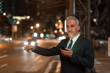 Businessman using mobile phone outdoors at night while waiting taxi
