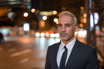 Fototapeta premium Portrait of handsome businessman wearing suit in city at night