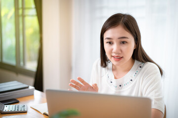 Happy Asian young woman working at home, working from home is the new working solution during the COVID-19 pandemic and able to increase working productivity. Asian beautiful girl using video call.