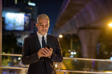 Businessman wearing suit in city at night while using mobile phone