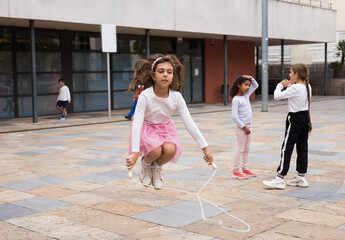 Happy schoolgirl jumping game by rubber band, kids friends on background