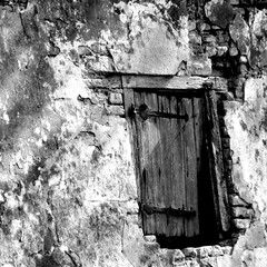 Close up of an old house wall with a small window in a forest in black and white