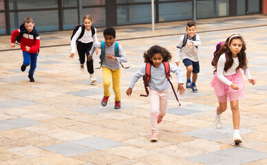 Portrait of cheerful tween boys and girls with school backpacks running in schoolyard in spring day.