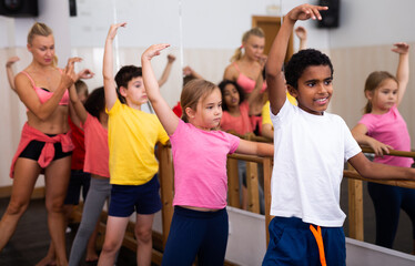 Smiling african boy practicing classic dance moves near ballet barre during group class © JackF