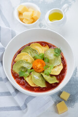 Bowl of ravioli with tomato sauce and parmesan cheese, vertical shot on a white concrete background