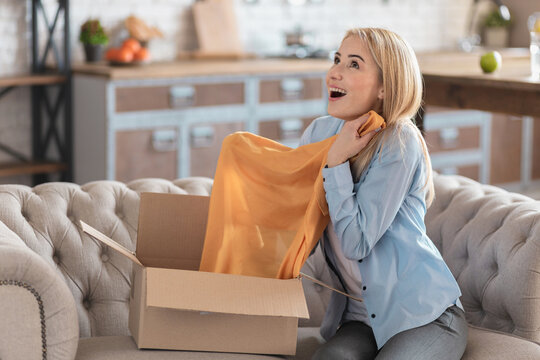 Happy young woman received a long-awaited parcel of clothes. Joyful woman opened a box with clothes