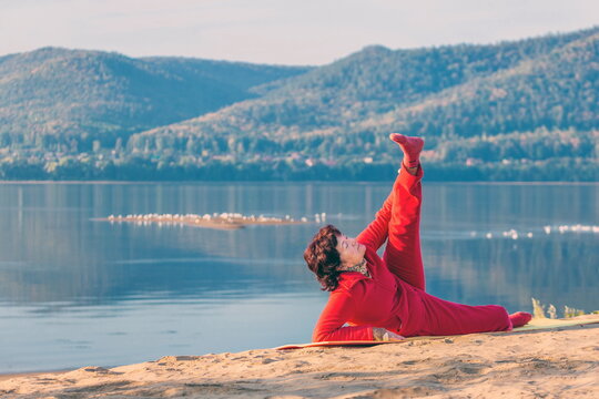 Beautiful Mature Woman Doing Gymnastics On A Sandy Beach On A Background Of Autumn Dawn.