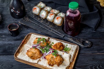 A set of fruit drinks, chicken skewers, rolls inside out with shrimps, flying fish caviar and cream cheese. Black background and black decor in Asian style.