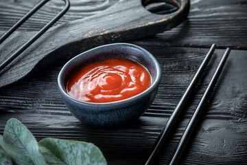 ketchup in a ceramic saucepan. Black wooden background and decor.