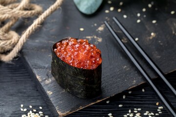 Gunkan Maki with red caviar. Black background and black decor.