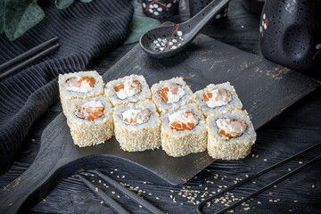 Uramaki roll inside out with cream cheese, bell pepper and shrimps. Covered with seasame seeds. Black background, black decor.