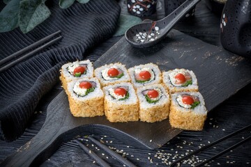 Uramaki roll inside out with lettuce, green onions and red fish and a drop of hot sauce. Covered with tuna shavings. Black background, black decor.
