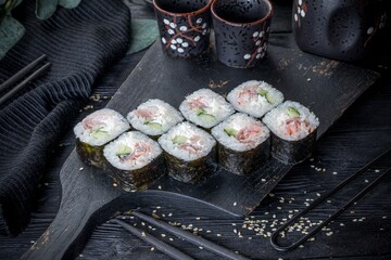 Classic sushi roll with fish, cucumber and cream cheese. Black background, black decor.