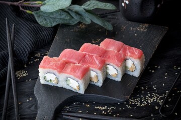 Uramaki roll inside out with tuna fillet, cream cheese, mushrooms and cucumber. Black background, black decor.