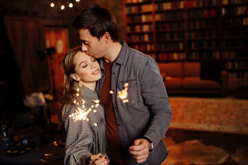 Beautiful couple hold sparklers in arms, adorable wife and charming husband enjoy festive mood, cozy winter holidays at home, New Year and Christmas celebration concept