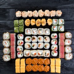 A large set of ten types of sushi rolls on a black wooden background. Top view.