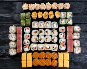 A large set of ten types of sushi rolls on a black wooden background. Top view.